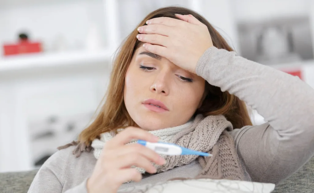 A Lady Holding A Thermometer And Her Forehead